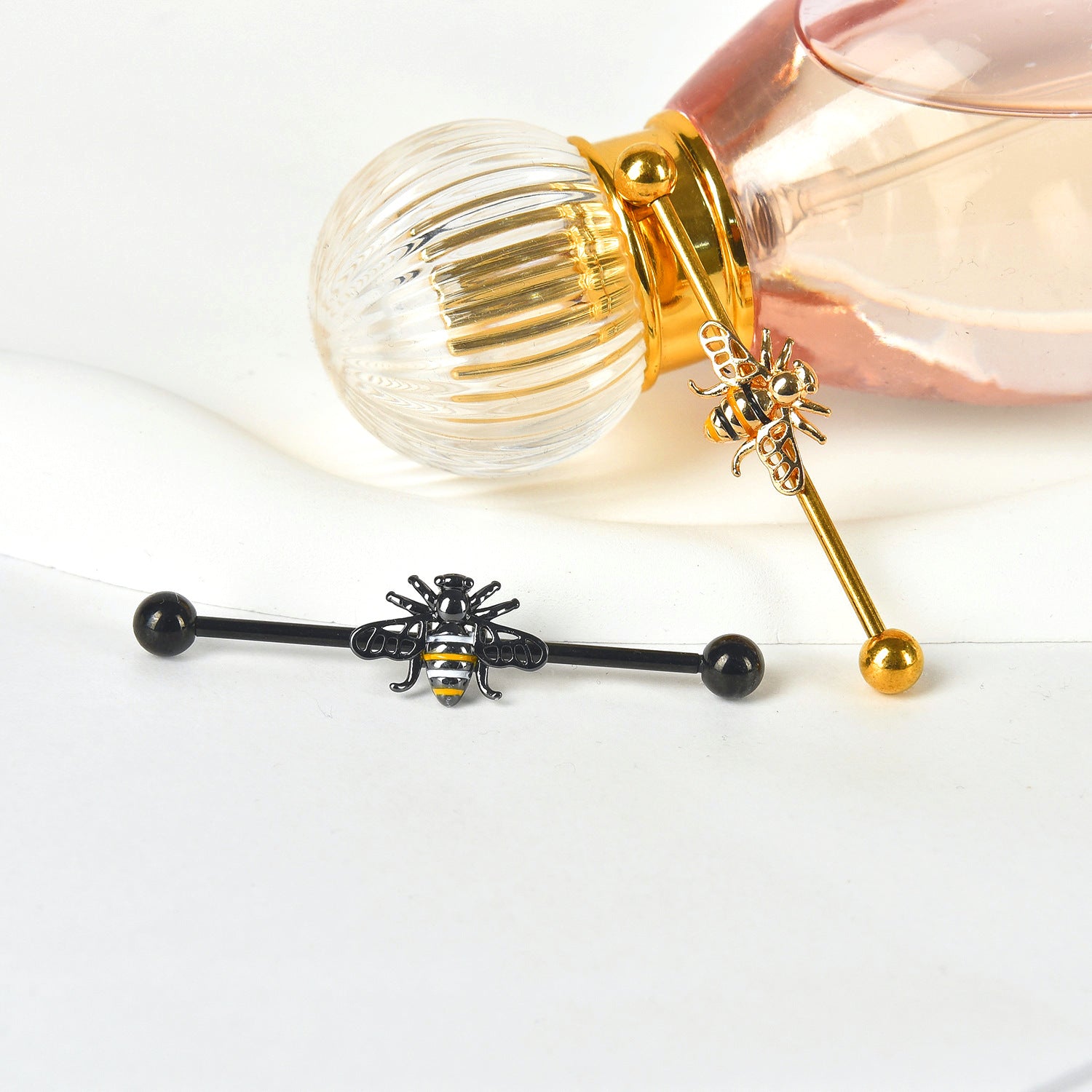 Black and gold bumblebee cartilage piercing bars styled with an elegant pink perfume bottle