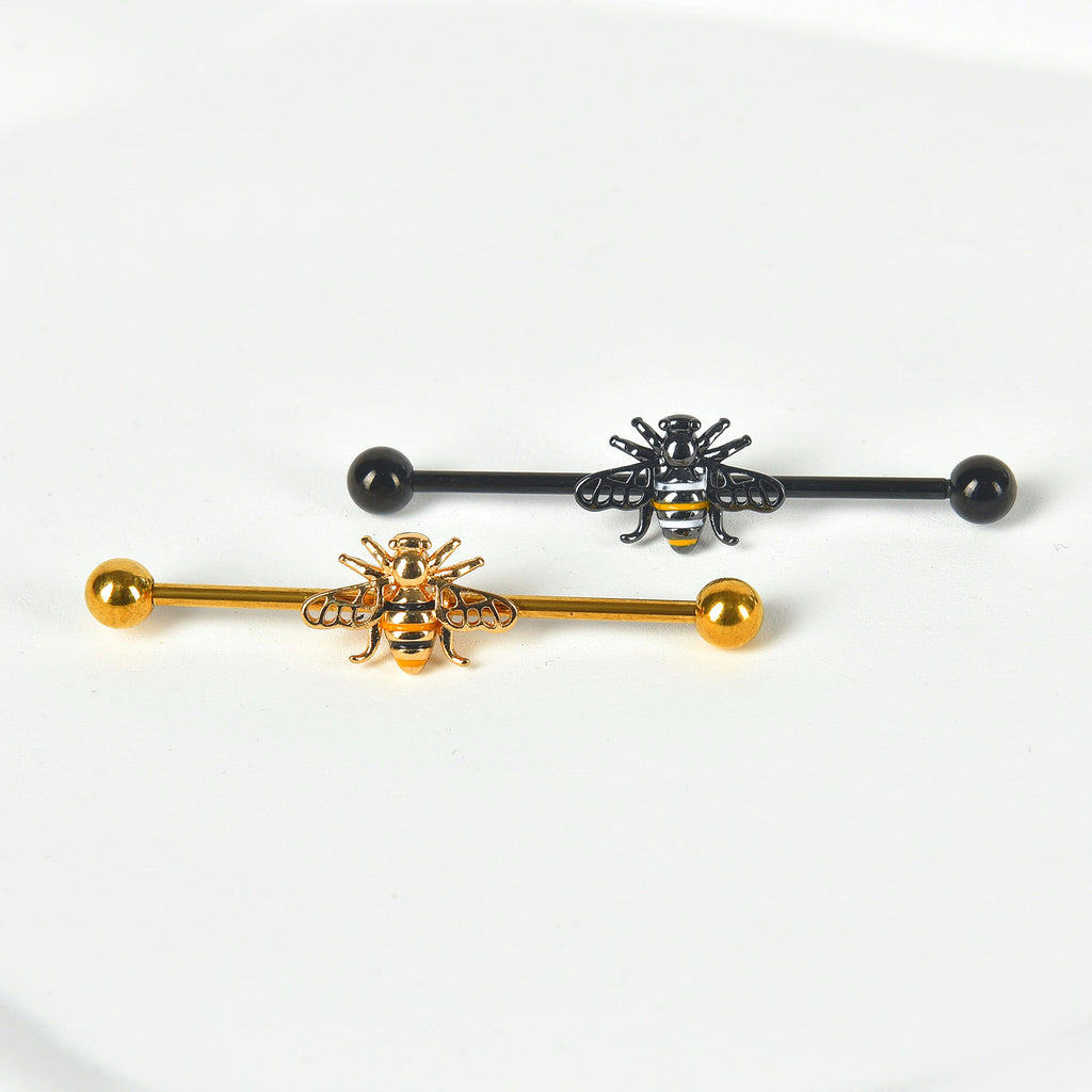 A gold honeybee industrial barbell and a black bee industrial piercing bar side by side on a clean white background